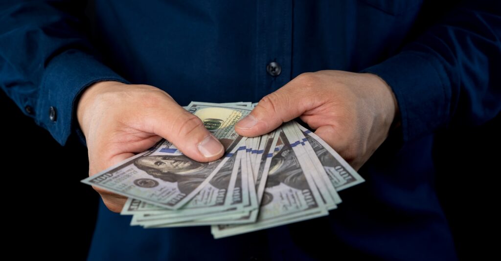 Big pile of money dollars in the hand. Close up of businessman counts money in hands. American Dollars Cash Money. 100 dollars banknotes in the background.