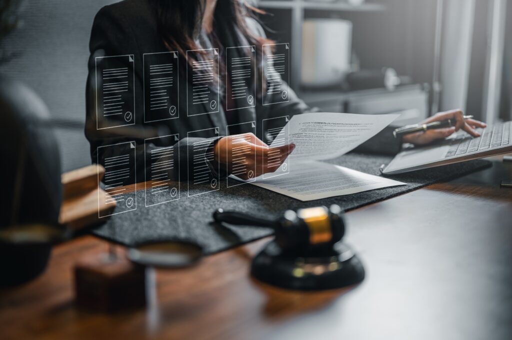 law, lawyer, judge, judgement, judgment, justice, advice, adviser, advocate, agreement. A woman is sitting with a stack of papers. She is holding a piece of paper and she is reading it.